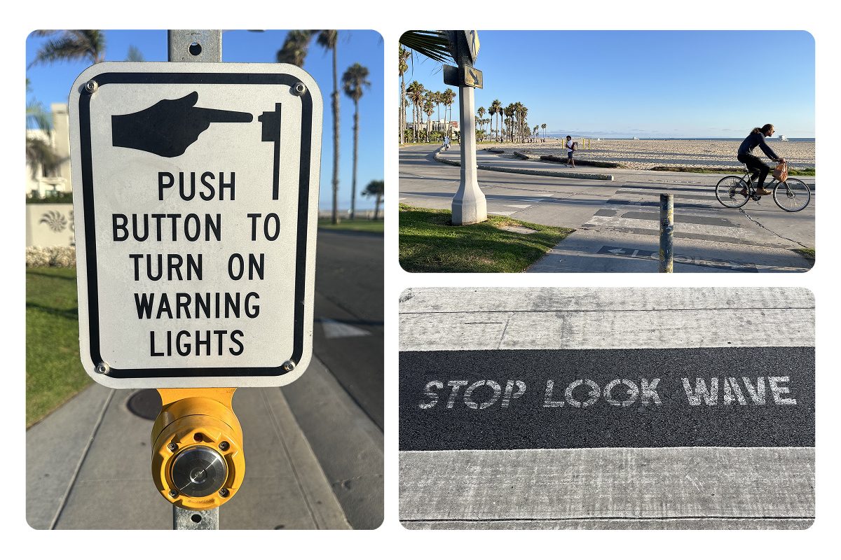 A roadside sign reading "push button to turn on warning lights" above a yellow button, the beach bike path crossing the walkway with a cyclist riding through, and "STOP LOOK WAVE" stenciled across the pavement.