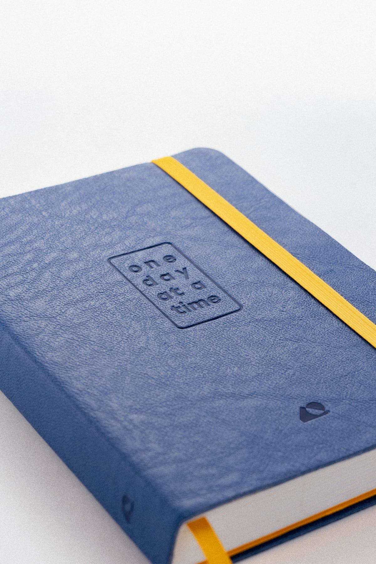 A close-up of the cover, "one day at a time" debossed into the blue beside the yellow elastic band.
