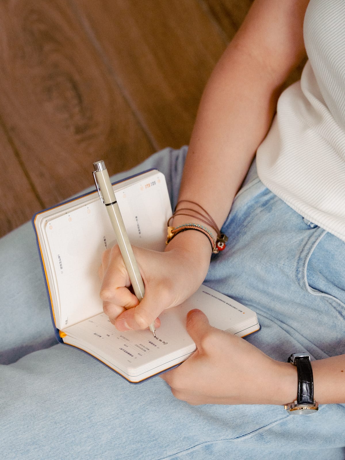 Someone sitting cross-legged, writing in the journal on their lap.