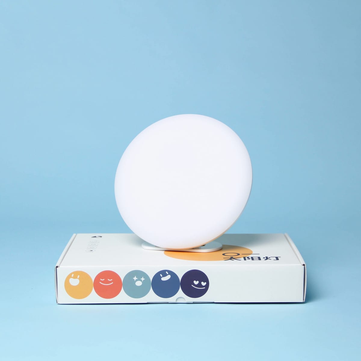The lamp resting on its box against a pale blue backdrop.